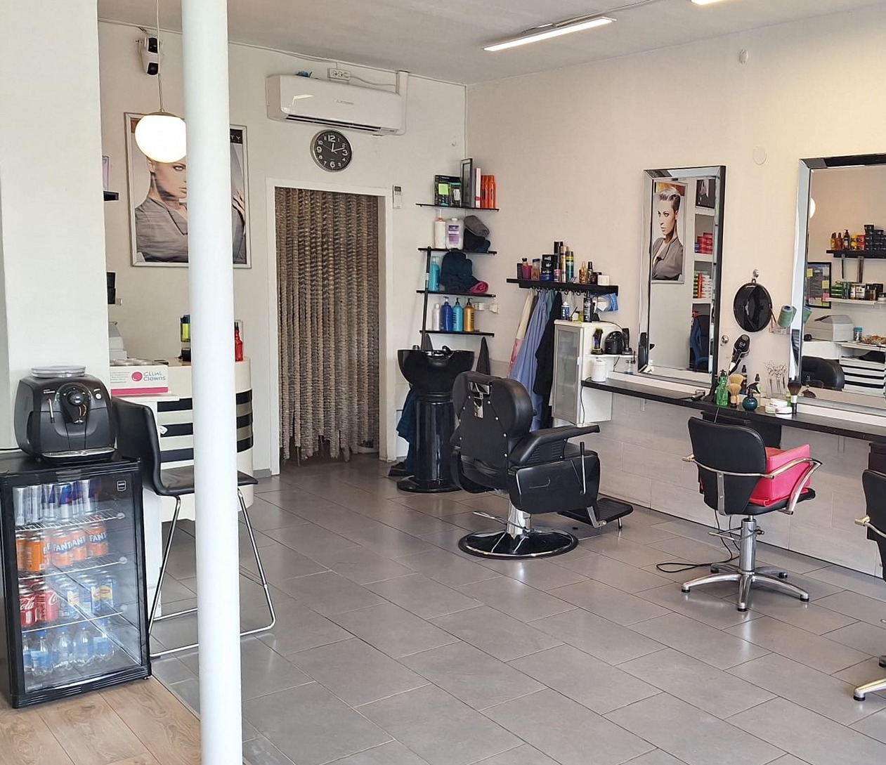 De zaak van Salon Milan van binnen: witte wanden, spiegels, zwarte kappersstoelen en één roze stoel