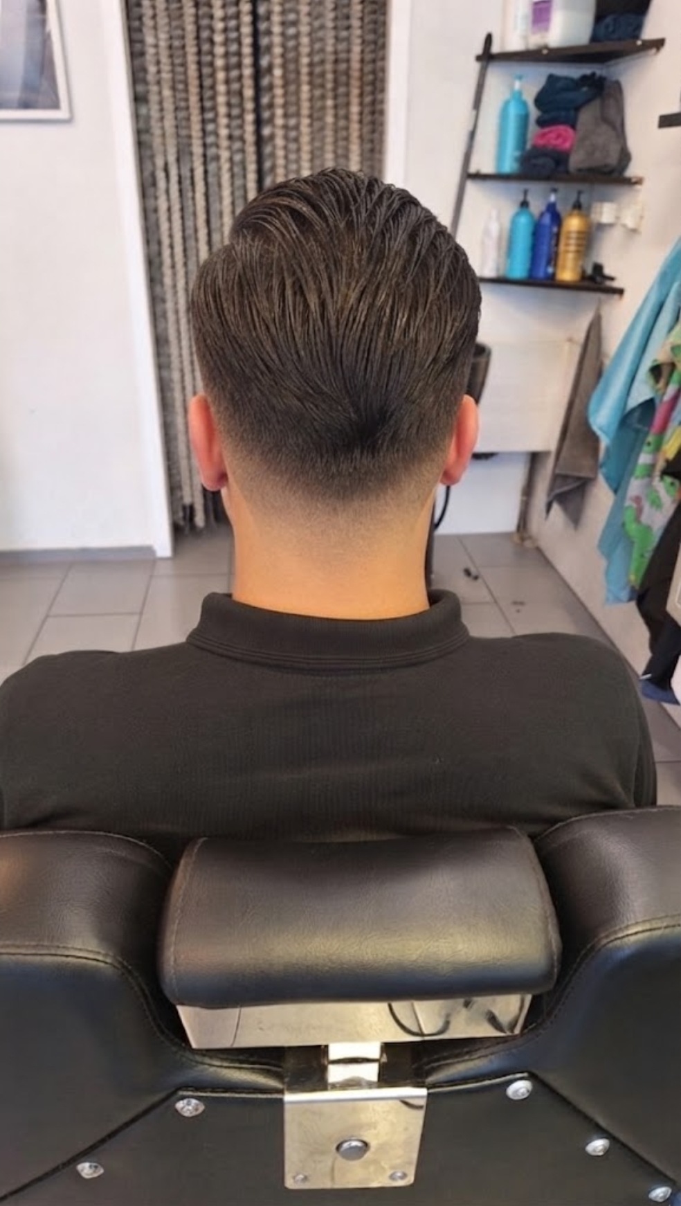 Achterhoofd van een klant met een verse fade, in een zwarte kappersstoel